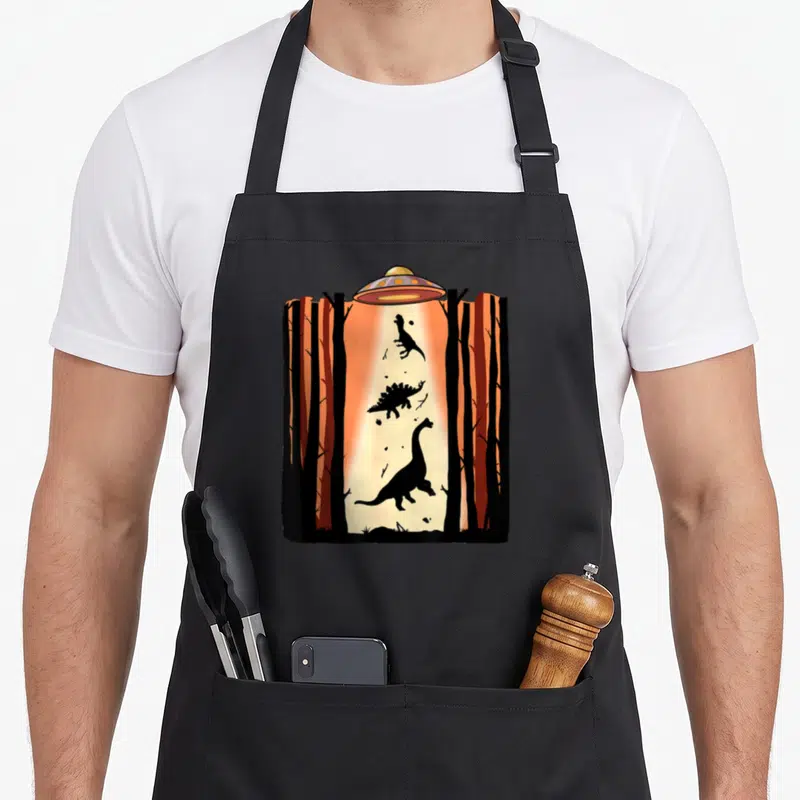 Tablier de cuisine noir avec illustration d'un ovin capturant des dinosaures dans une forêt orange.