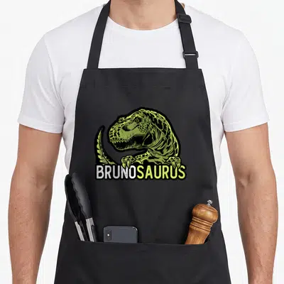 Tablier de cuisine noir avec illustration d'un T-Rex vert lime et du texte BRUNOSAURUS en blanc et vert sous la bête.