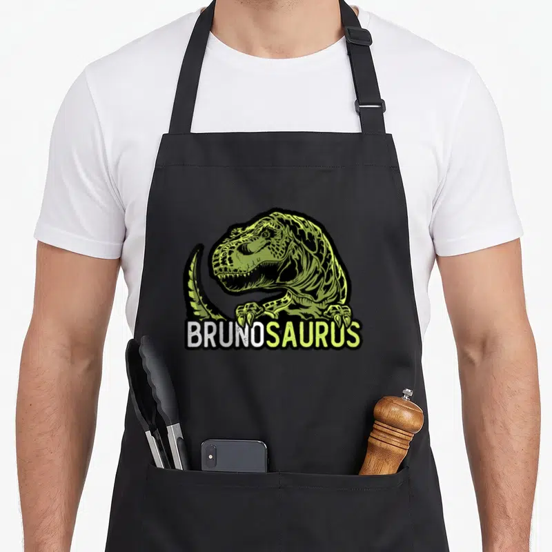 Tablier de cuisine noir avec illustration d'un T-Rex vert lime et du texte BRUNOSAURUS en blanc et vert sous la bête.