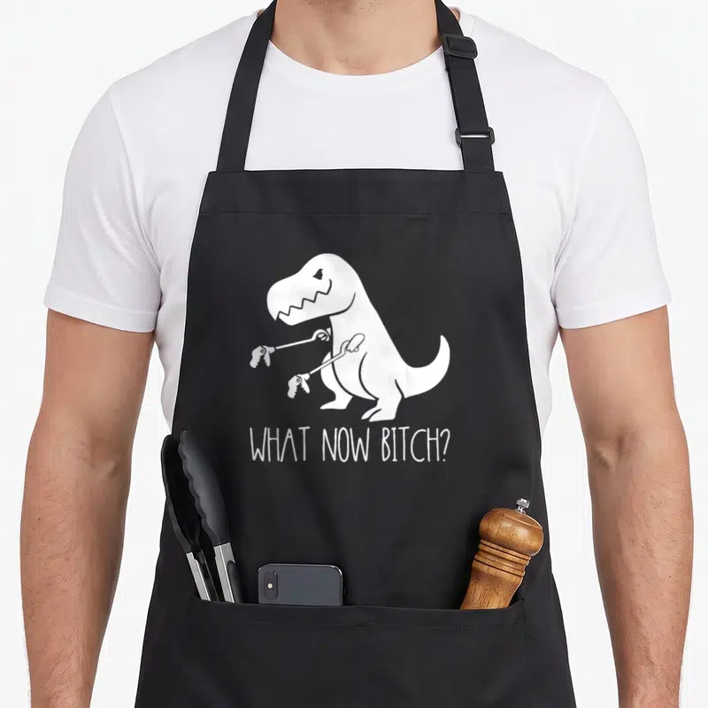 Tablier de cuisine noir avec illustration blanche d'un T Rex aux bras de mouches et texte What Now Bitch.