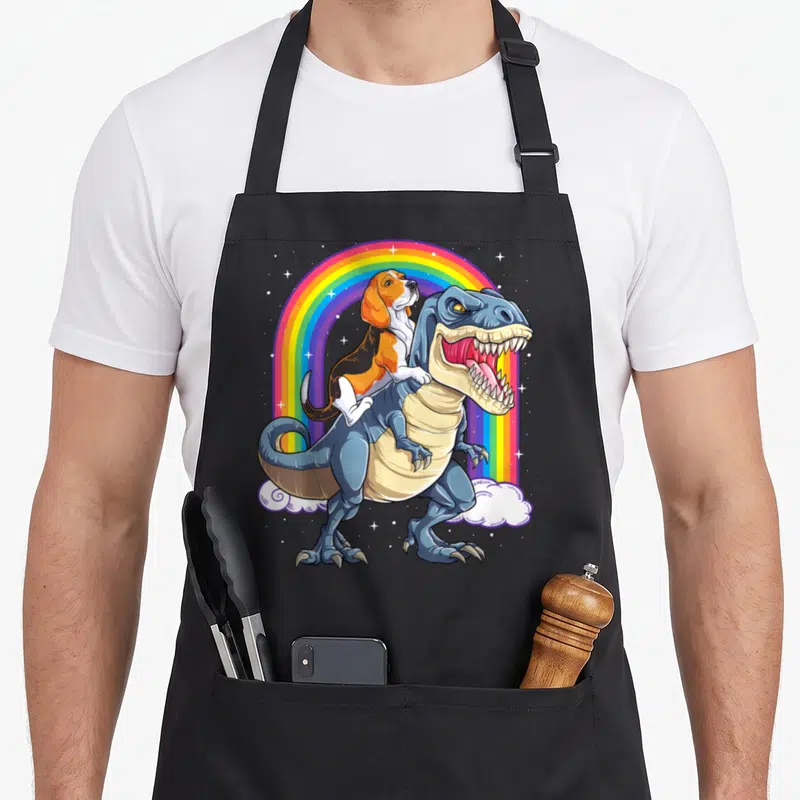 Tablier de cuisine noir avec illustration d'un beagle montant un t-rex sous un arc-en-ciel étoilé