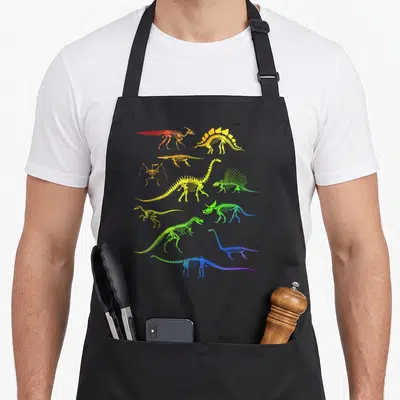 Tablier de cuisine noir avec des squelettes de dinosaures aux couleurs arc-en-ciel disposés en grille.