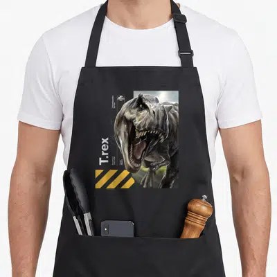 Tablier de cuisine noir avec illustration réaliste d'un T.rex aux dents acérées et bandes jaunes de signalisation.