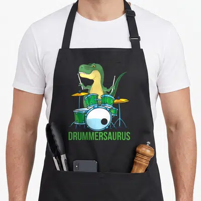 Tablier de cuisine noir avec un T Rex vert jouant de la batterie sous le mot Drummersaurus en lettres vertes.
