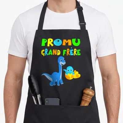 Tablier de cuisine noir avec dinosaure bleu et texte Promu grand frère en lettres multicolores.