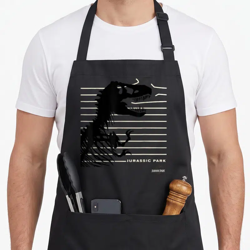 Tablier de cuisine noir avec silhouette T-Rex et lignes blanches évoquant une clôture brisée