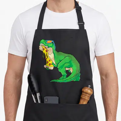 Tablier de cuisine noir avec un dinosaure vert aux lunettes bleues mangeant une pizza au pepperoni.