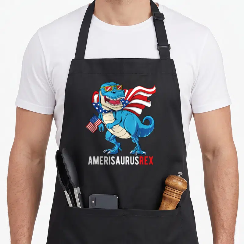 Tablier de cuisine noir avec un dinosaure bleu portant des lunettes de soleil et une cape aux étoiles américaines.
