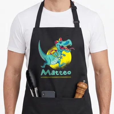 Tablier de cuisine noir avec un dinosaure turquoise portant une casquette et le nom Matteo imprimé en dessous.