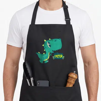 Tablier de cuisine noir avec un dinosaure vert mignon et le nom Viktor dans une bulle de dialogue jaune.