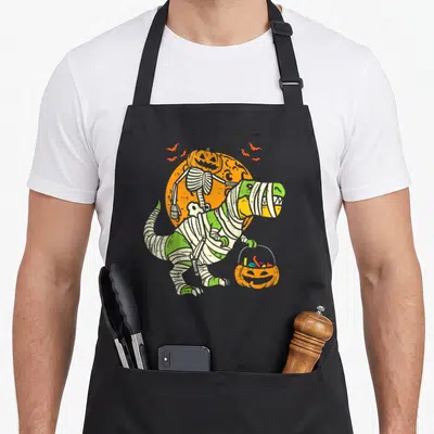 Tablier de cuisine noir avec illustration T-Rex mummy et squelette citrouille sur fond orange.