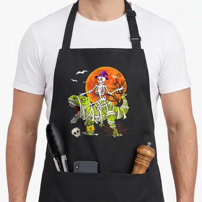 Tablier de cuisine noir avec un squelette en chapeau violet montant un dinosaure vert bandé devant une lune orange.