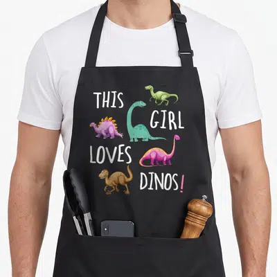 Tablier de cuisine noir avec quatre dinosaures colorés et le texte This Girl Loves Dinos.