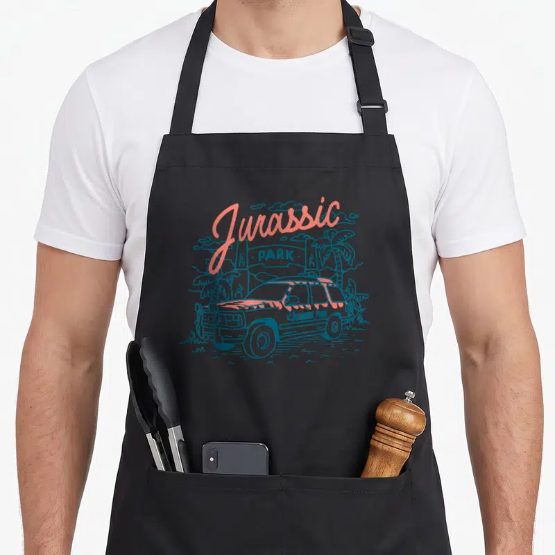 Tablier de cuisine noir avec illustration d'une jeep et d'une enseigne Jurassic Park en dessin au trait coloré.