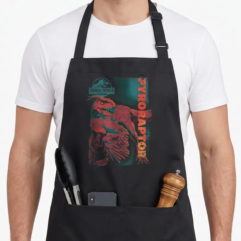 Tablier de cuisine noir avec illustration d'un Pyroraptor rouge et texte vertical orange Jurassic World Dominion