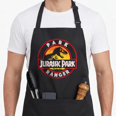Tablier de cuisine noir avec logo circulaire rouge et noir représentant un dinosaure sur fond orange.