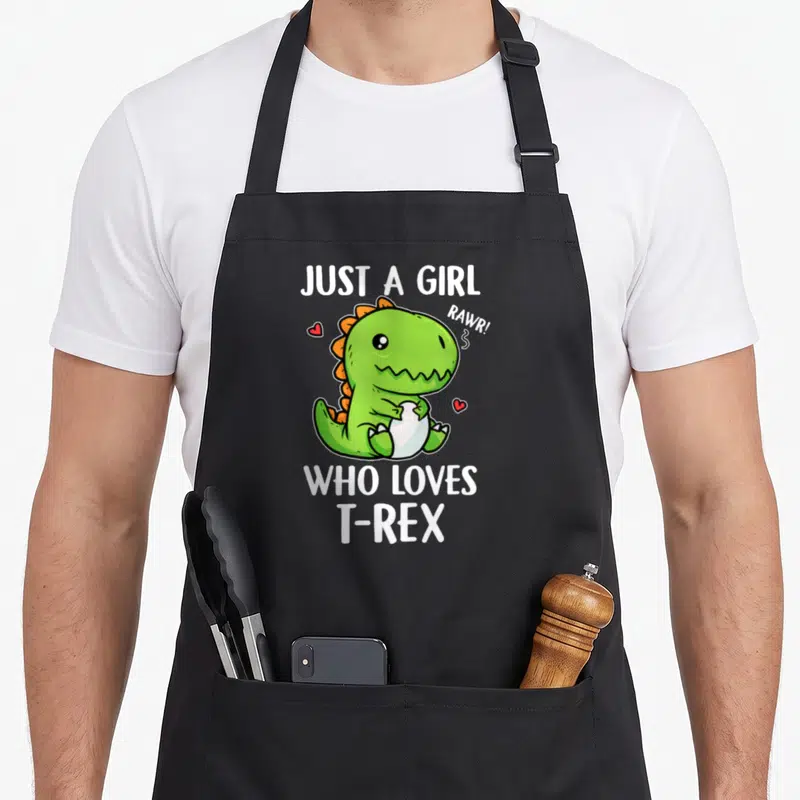 Tablier de cuisine noir avec un T-Rex vert tenant un œuf et le texte Just A Girl Who Loves T-Rex Rawr.