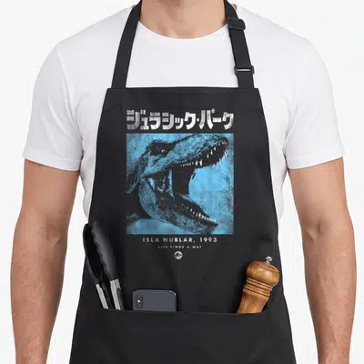 Tablier de cuisine noir avec tête de dinosaure bleue et texte japonais en haut, Isla Nublar 1993 en bas.