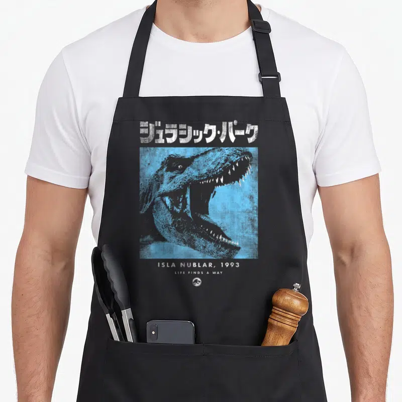 Tablier de cuisine noir avec tête de dinosaure bleue et texte japonais en haut, Isla Nublar 1993 en bas.