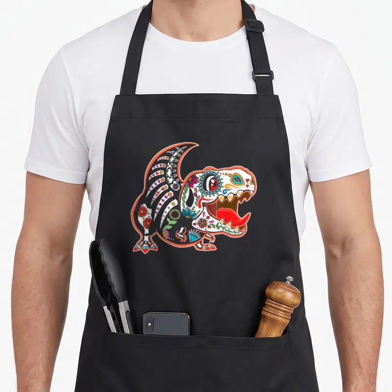 Tablier de cuisine noir avec un T rex dia de los muertos aux couleurs vives et motifs floraux.
