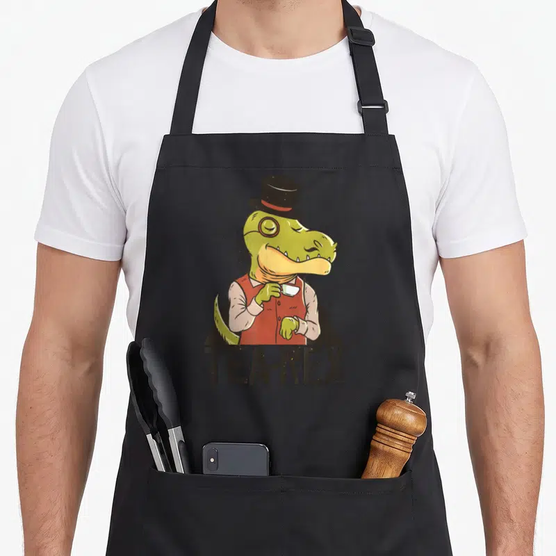 Tablier de cuisine noir avec illustration d'un T-Rex monocle chapeau haut de forme tenant une tasse et texte Tea-Rex.