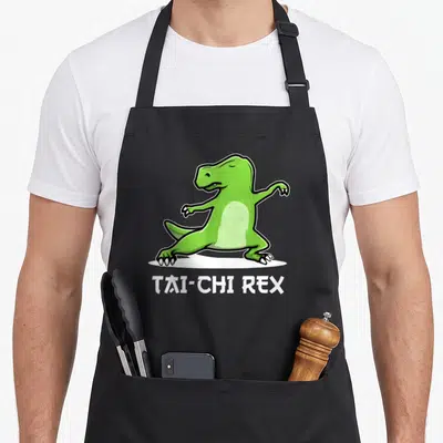 Tablier de cuisine noir avec un T-Rex vert en posture de Tai Chi et le texte TAI-CHI REX en blanc.