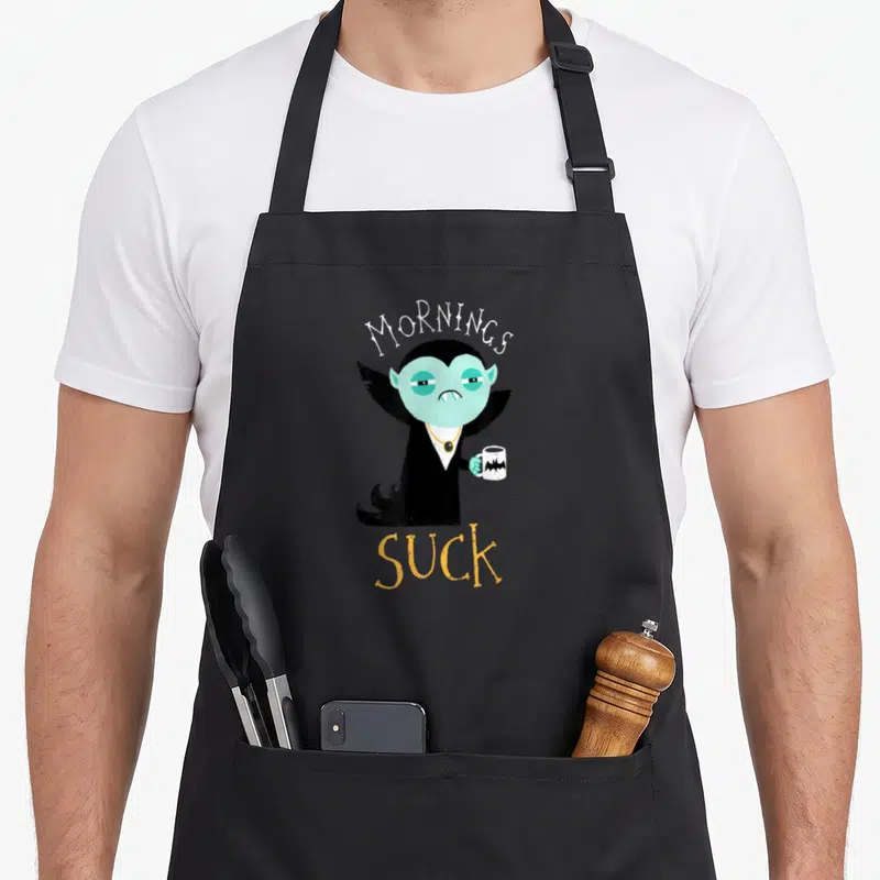 Tablier de cuisine noir avec illustration vampire vert et texte Mornings Suck en blanc et orange.