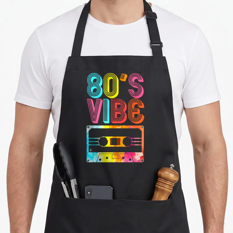Tablier de cuisine noir avec inscription ambiance des années 80 et illustration de cassette aux couleurs vives.