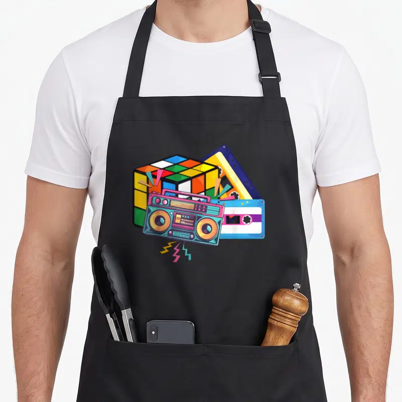 Tablier de cuisine noir avec illustration d'une cassette, d'un boombox et d'un cube Rubik colorés.