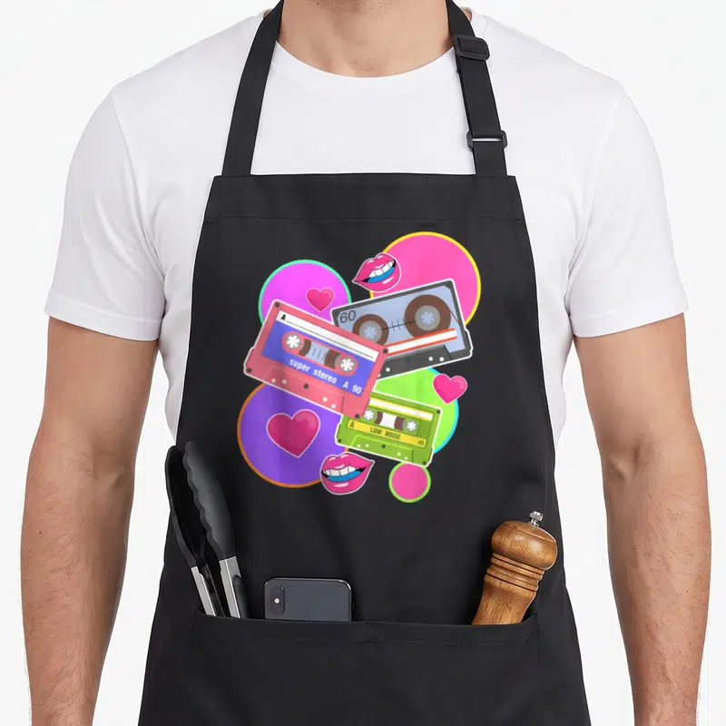 Tablier de cuisine noir avec illustration colorée de trois cassettes audio vintage, lèvres roses et cœurs sur fond de cercles géométriques.