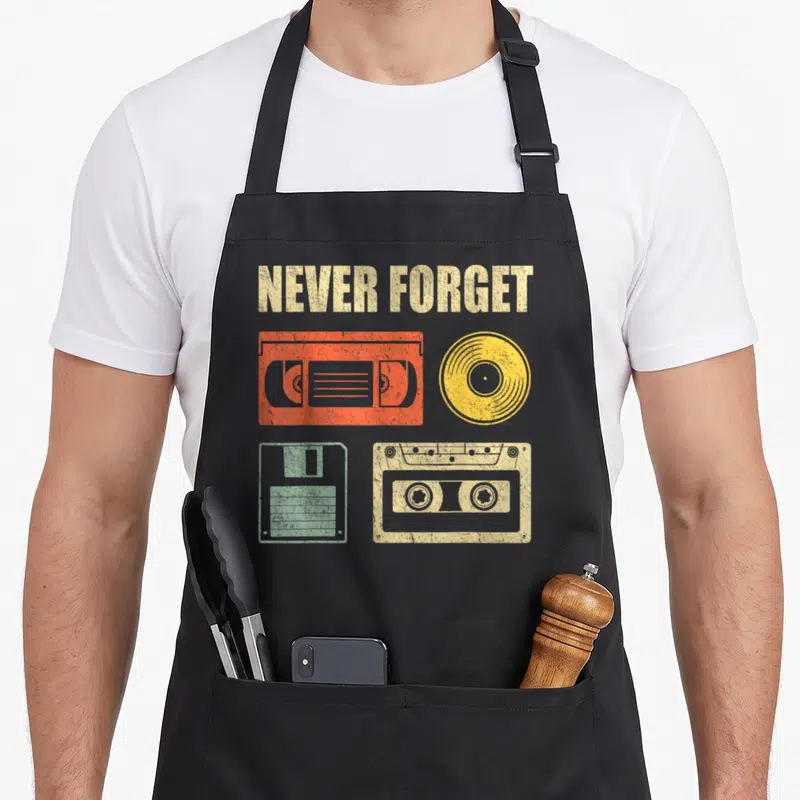 Tablier de cuisine noir avec illustration vintage de cassettes audio, vinyle jaune et disquette mint sur fond uni.