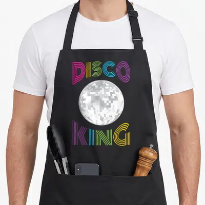 Tablier de cuisine noir avec une boule à facettes argentée et les mots Disco King en lettres rayées colorées.