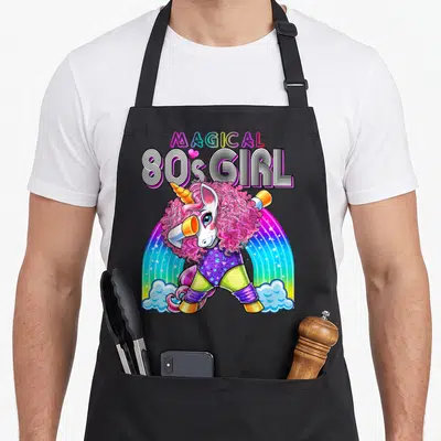 Tablier de cuisine noir avec licorne rose en train de faire le dab sous un arc-en-ciel coloré et du texte rétro.