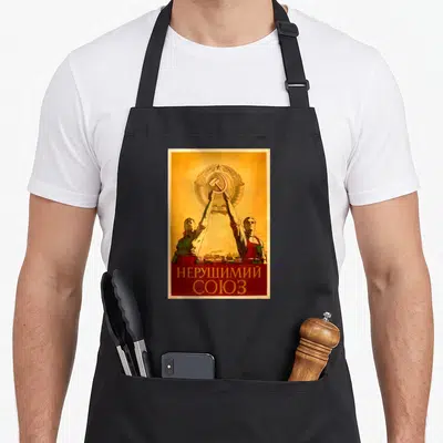 Tablier de cuisine noir avec une illustration vintage représentant deux travailleurs tenant un emblème soviétique au-dessus d'une ville.