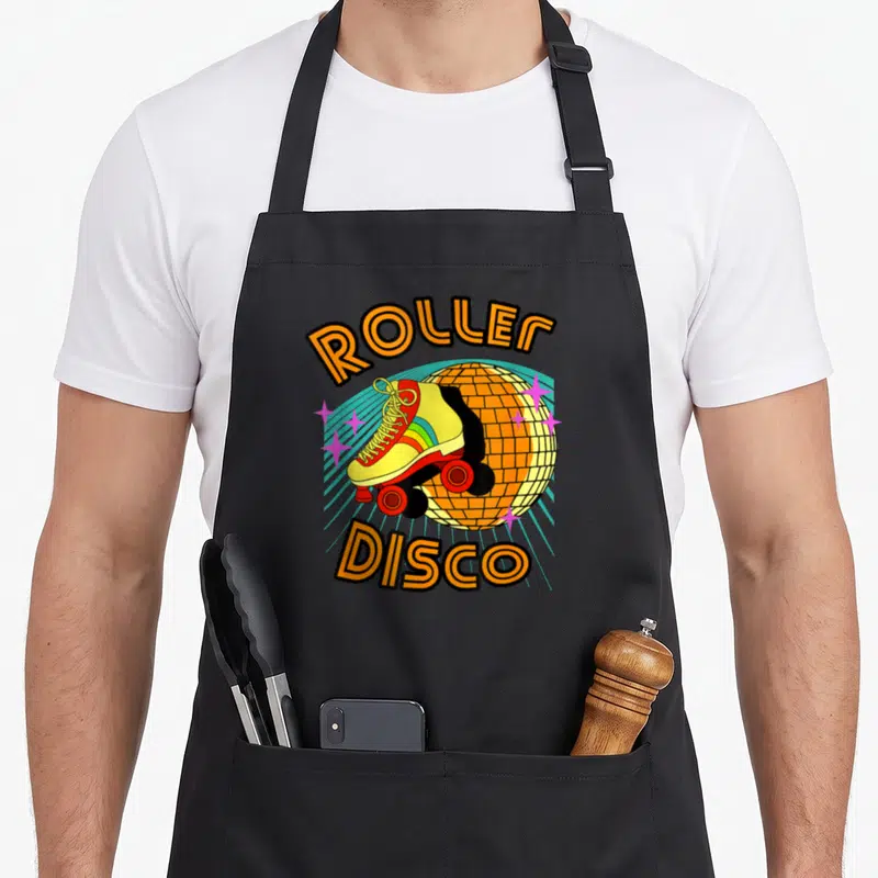 Tablier de cuisine noir avec un patin à roulettes jaune, une boule disco et l'inscription Roller Disco colorée.