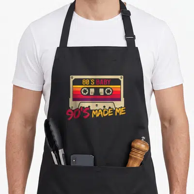 Tablier de cuisine noir avec une illustration de cassette audio colorée et un texte retro en jaune et rouge.