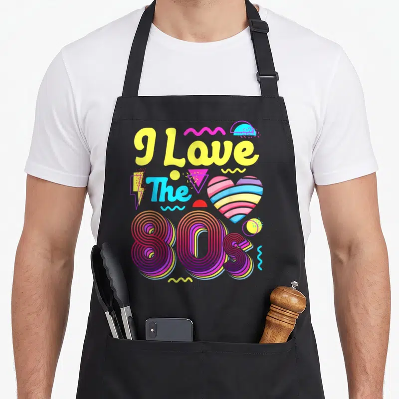 Tablier de cuisine noir avec le texte I Love The 80s en lettres jaunes et un cœur aux bandes arc-en-ciel.