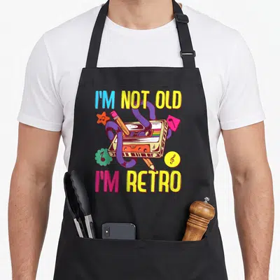 Tablier de cuisine noir avec une illustration de cassette audio et le texte I'm Not Old I'm Retro en lettres colorées.