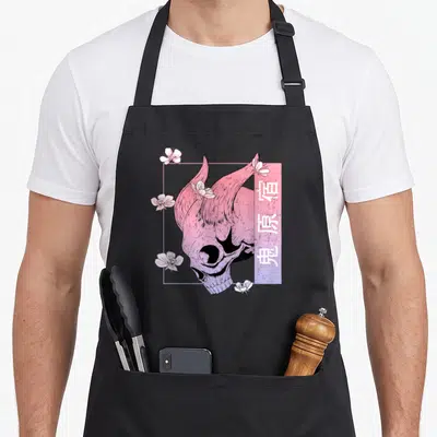 Tablier de cuisine noir avec un crâne de démon rose, des fleurs blanches et des symboles japonais dans un cadre géométrique pastel.
