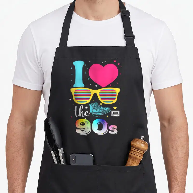 Tablier de cuisine noir avec lunettes jaunes, cœur rose et texte J'aime les 90s coloré.