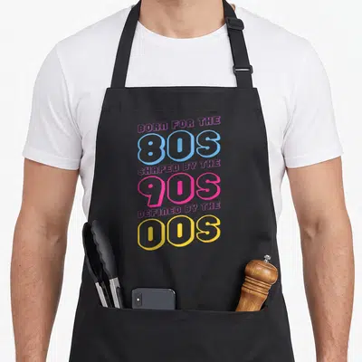 Tablier de cuisine noir avec inscription colorée célébrant les années 80, 90 et 00 en typographie rétro.
