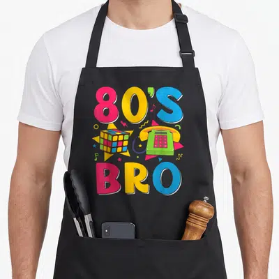 Tablier de cuisine noir avec typographie 80's Bro, téléphone vert et cube de Rubik coloré sur fond gris uni.