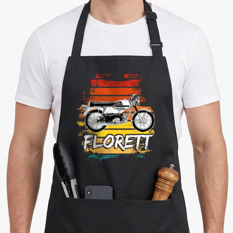 Tablier de cuisine noir avec illustration vintage d'un cyclomoteur Kreidler Florettt sur fond rayé orange et jaune.