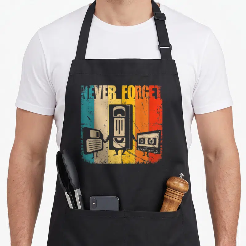 Tablier de cuisine noir avec illustration vintage disquette VHS et cassette sur fond rayé multicolore.
