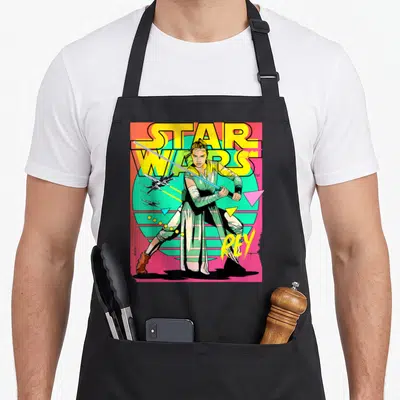 Tablier de cuisine noir avec illustration rétro de Rey tenant un sabre laser sous le logo Star Wars en jaune vif.