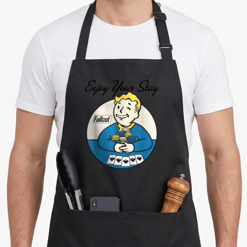 Tablier de cuisine noir avec illustration circulaire de Vault Boy tenant des cartes à jouer et des jetons de poker.