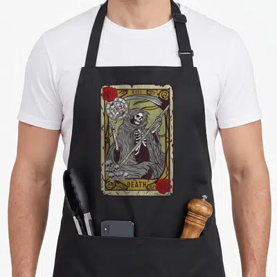 Tablier de cuisine noir avec illustration vintage d'une carte de tarot montrant une faucheuse squelettique tenant une faux et un sablier.