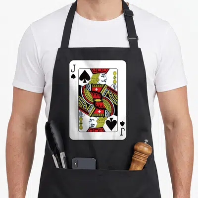Tablier de cuisine noir avec une grande carte à jouer représentant un valet de pique aux couleurs vives.