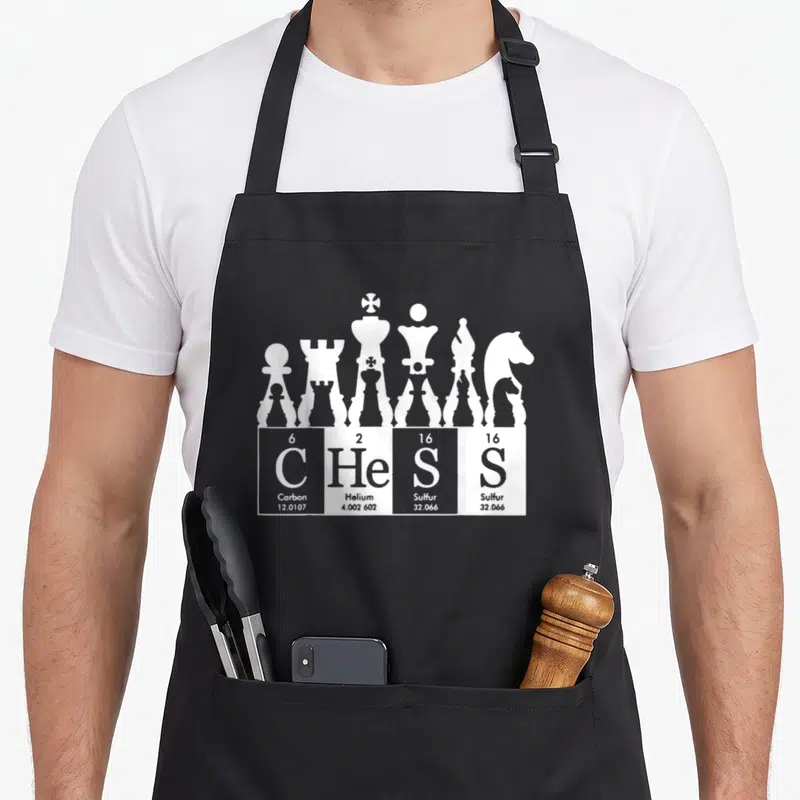 Tablier de cuisine noir avec des pièces d'échecs blanches et le mot CHeSS en éléments chimiques.