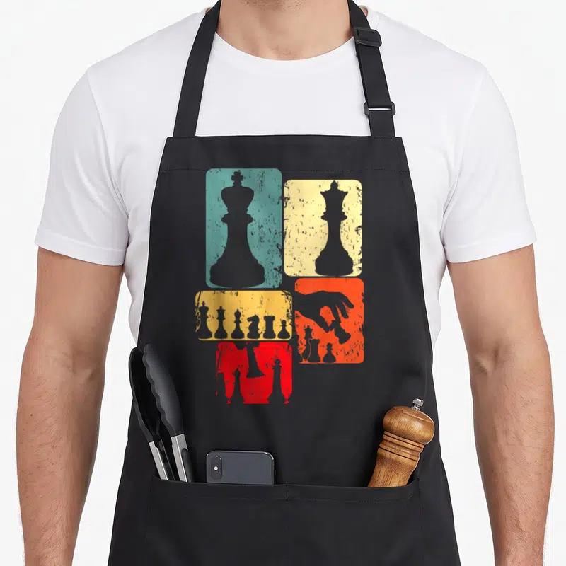 Tablier de cuisine noir avec silhouettes de pièces d'échecs sur rectangles turquoise, jaune, orange et rouge à effet vieilli.